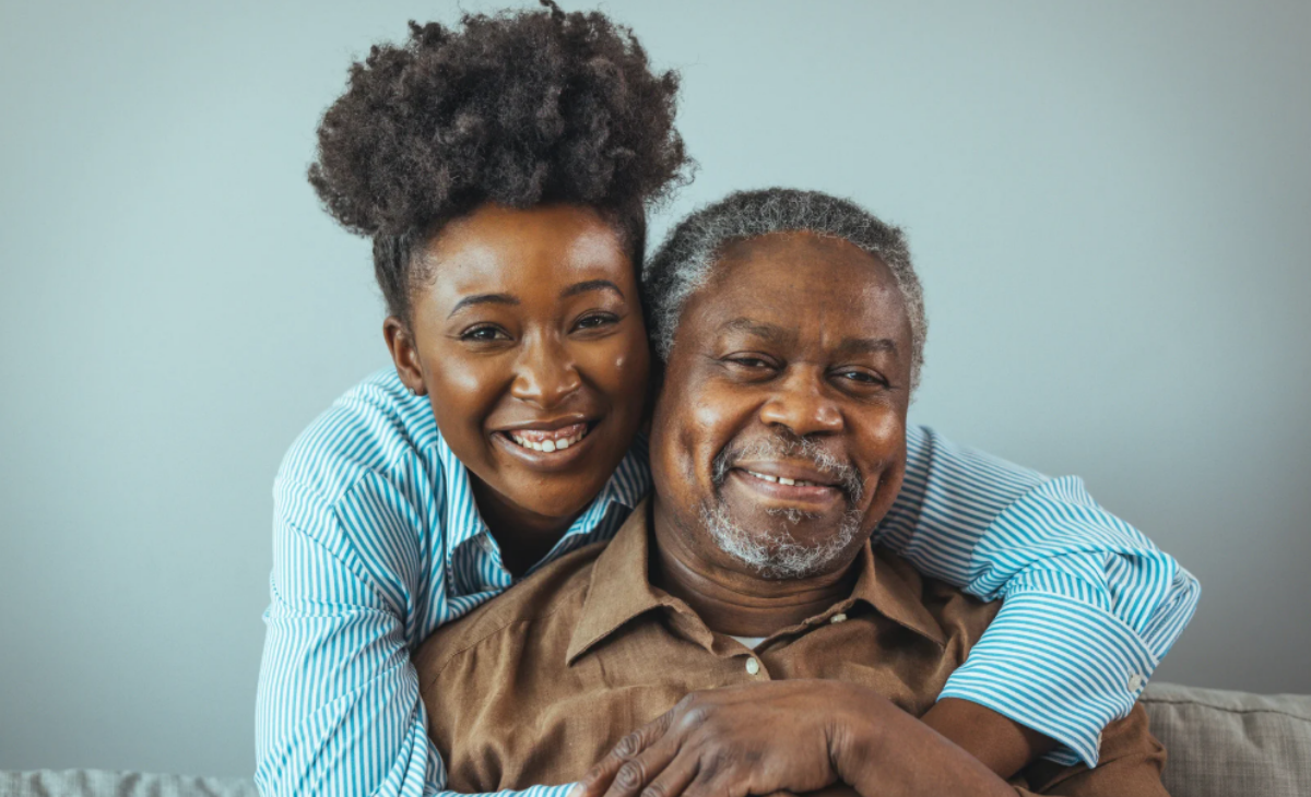 Daughter hugging her elderly father and smiling together at home, symbolizing love, family support, and the comfort of assisted living.