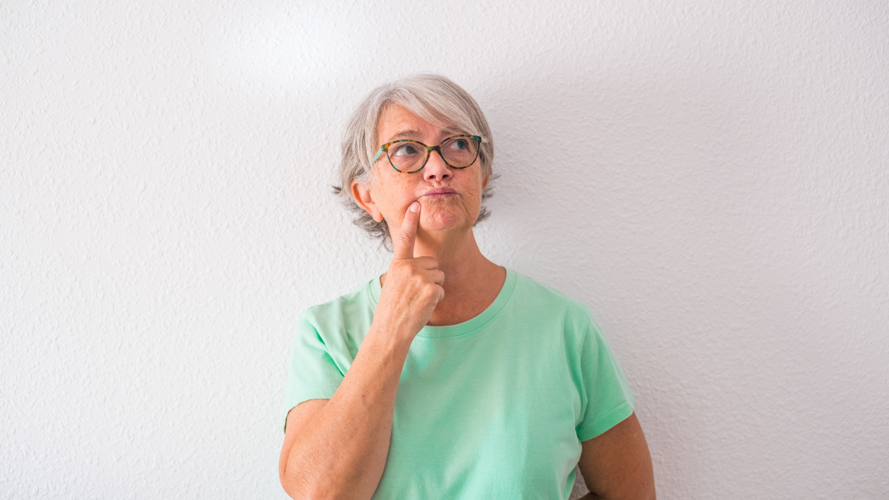 Senior woman thoughtfully considering the question, is it time for assisted living, while standing against a white wall.
