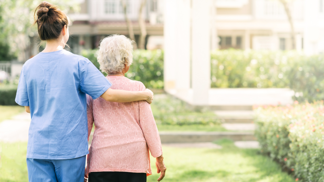 Caregiver walking with a senior woman outdoors, representing who qualifies for assisted living and the support available in assisted living communities.