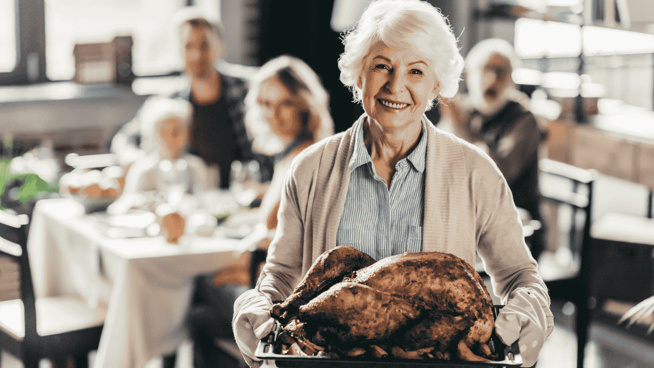 Smiling elderly woman presents a roasted turkey during a family thanksgiving holiday feast in a cozy dining room.