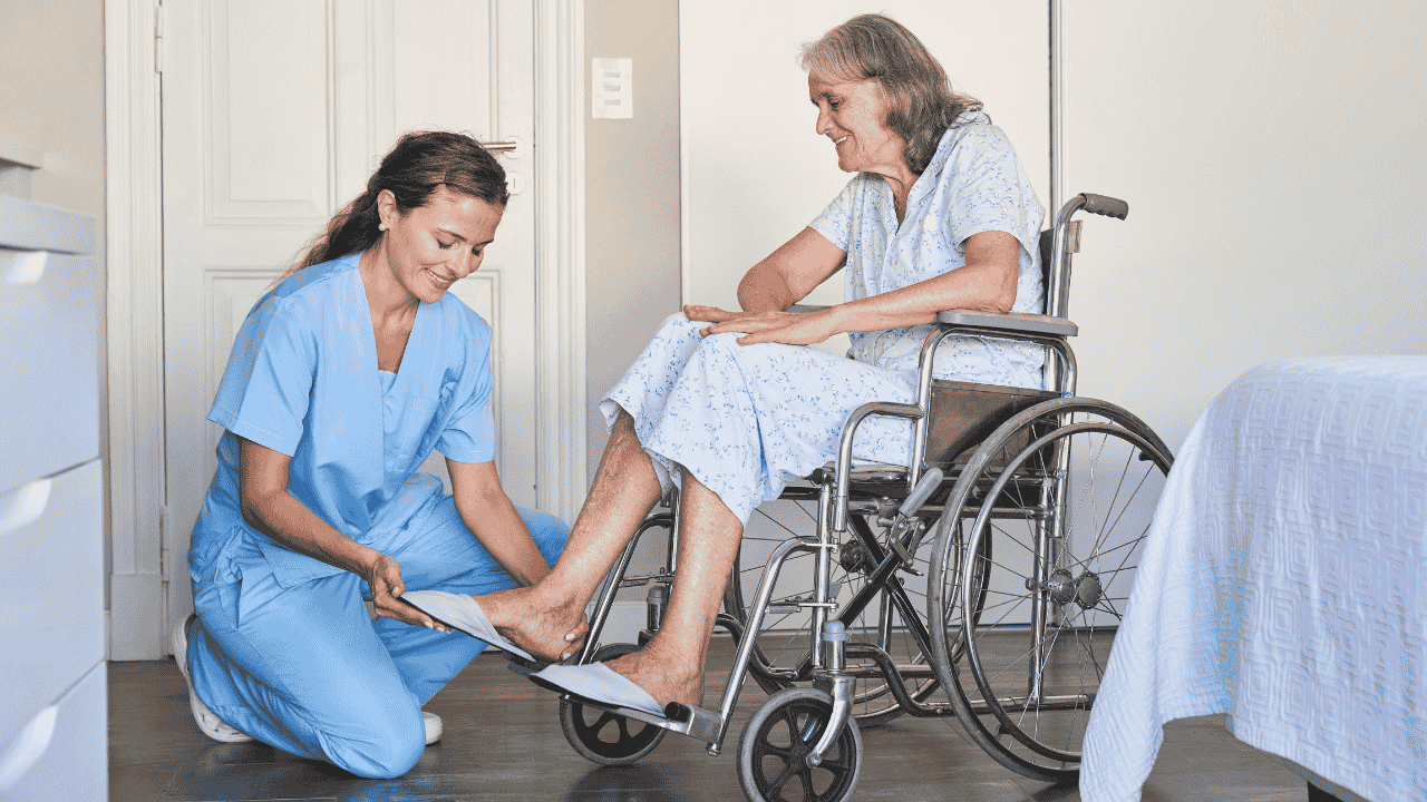 A caregiver helps an elderly woman in a wheelchair put on slippers, showing compassionate support and practical tips for taking care of elderly.