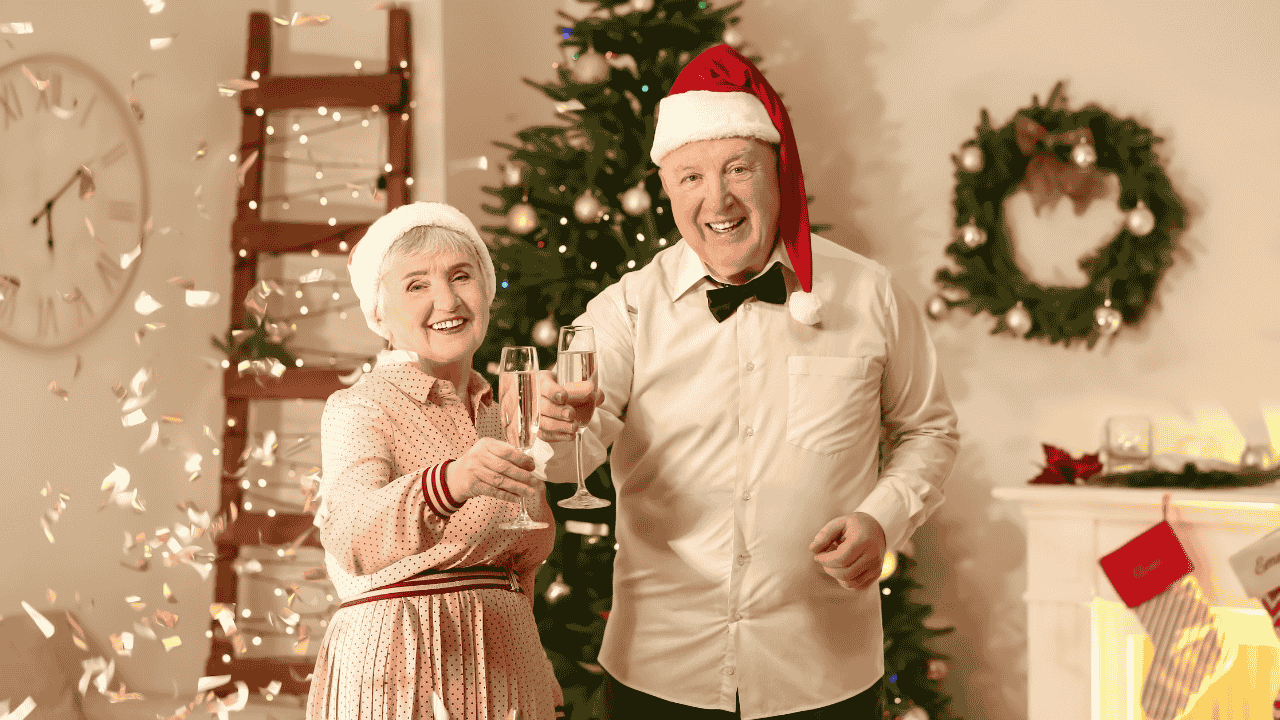 Smiling senior couple in Santa hats toasting with champagne by a Christmas tree, celebrating a warm keep calm christmas moment.